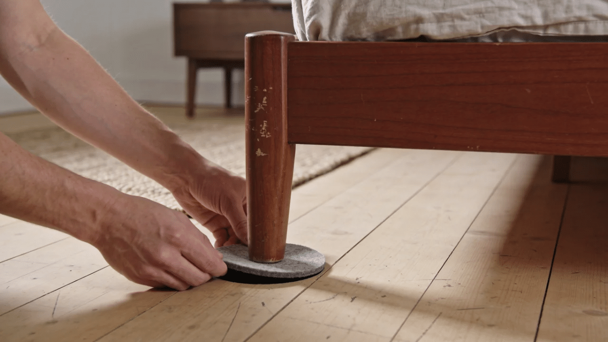 homeowner placing a rubber furniture cup beneath a bed leg to prevent squeaks sliding and floor scratches