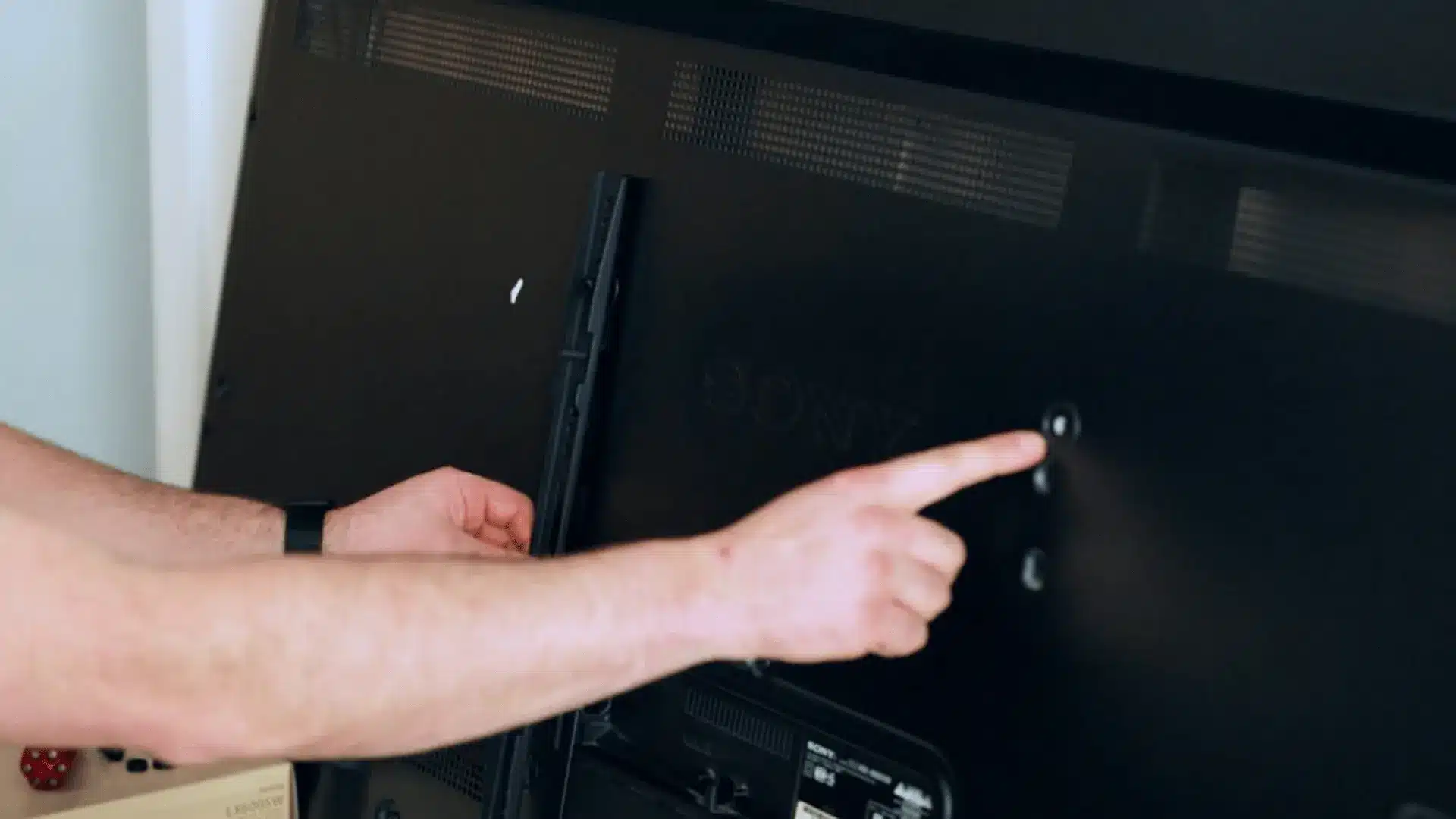 hand checking mounting holes on the back of a television