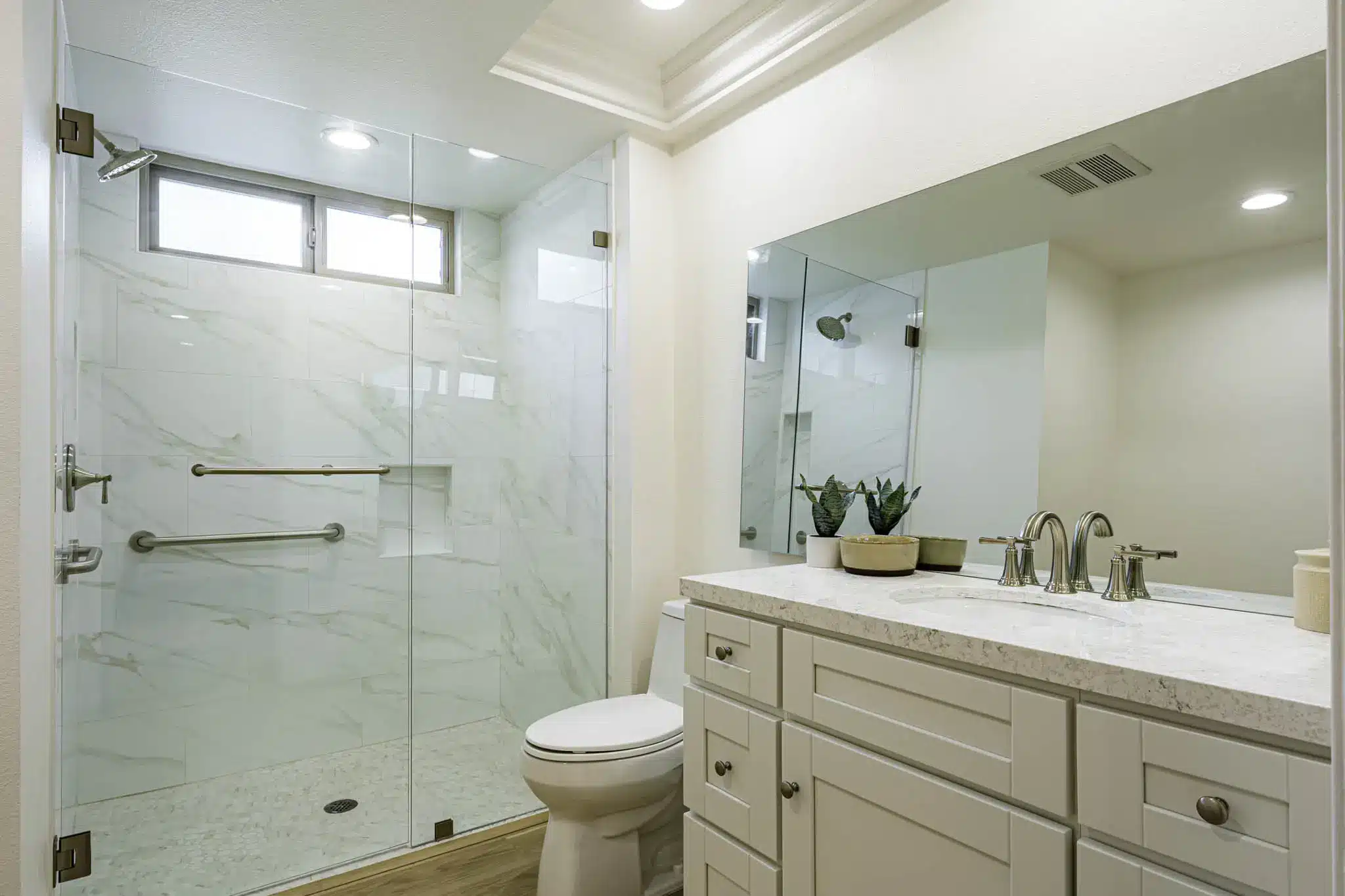 Modern bathroom with marble shower, white cabinetry, and potted plants on light countertop