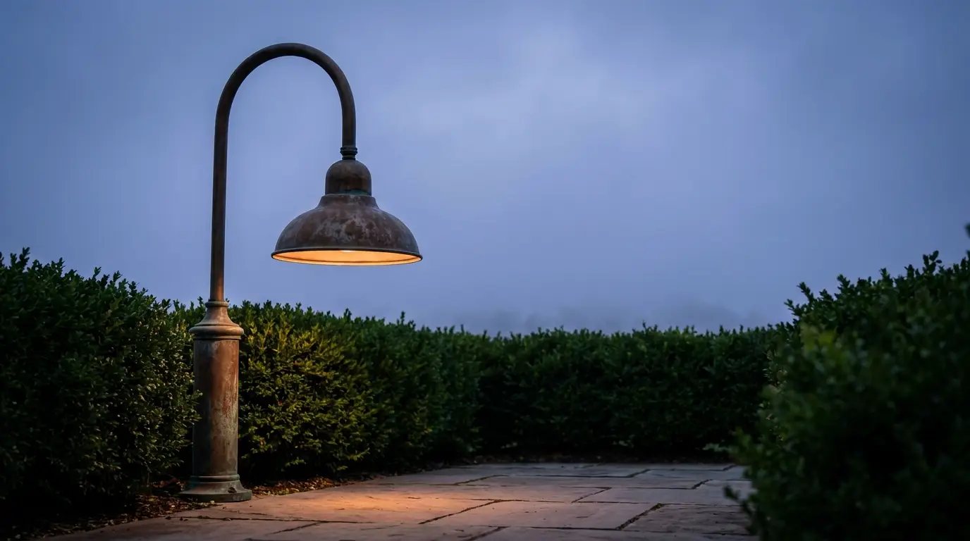 Rustic outdoor lamp illuminating paved walkway surrounded by hedges at dusk