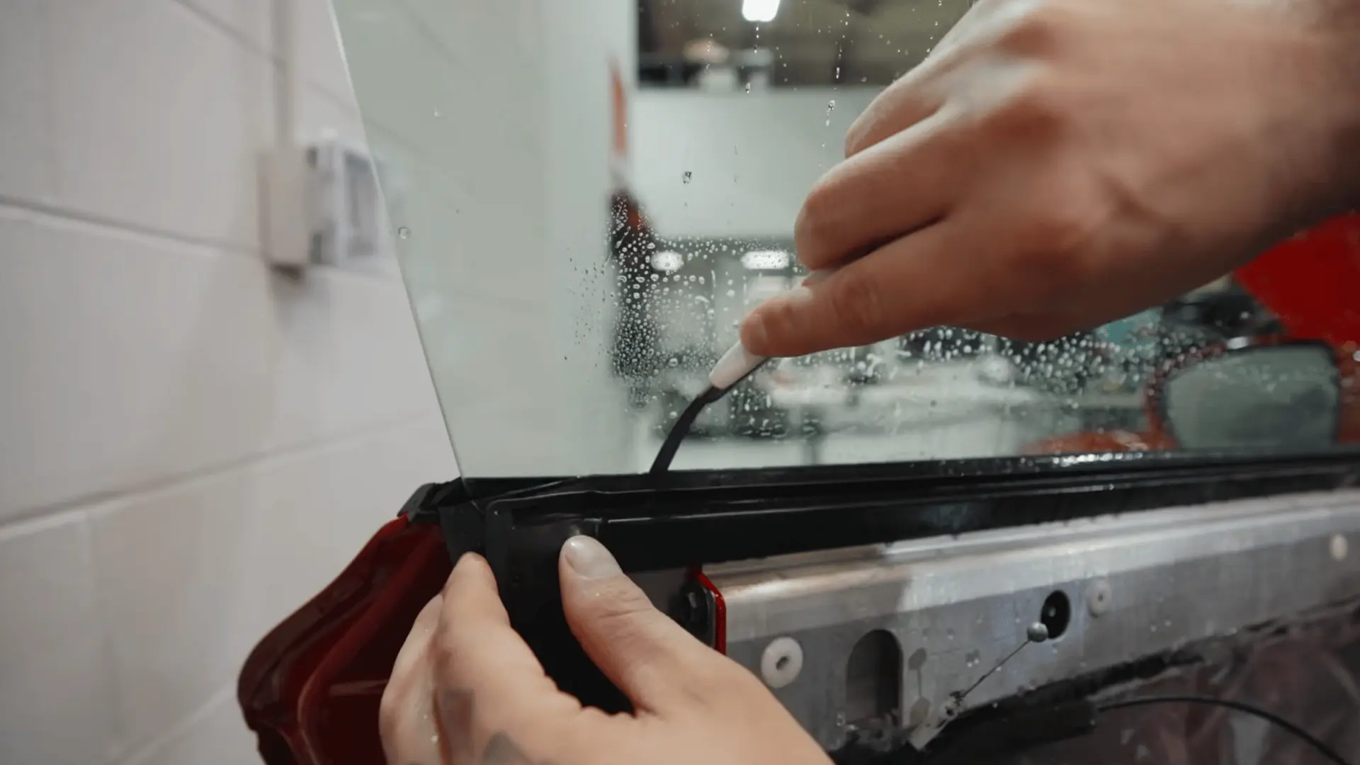 hands use a white tool to tuck black tint film along the lower edge of a wet car window with the door panel exposed