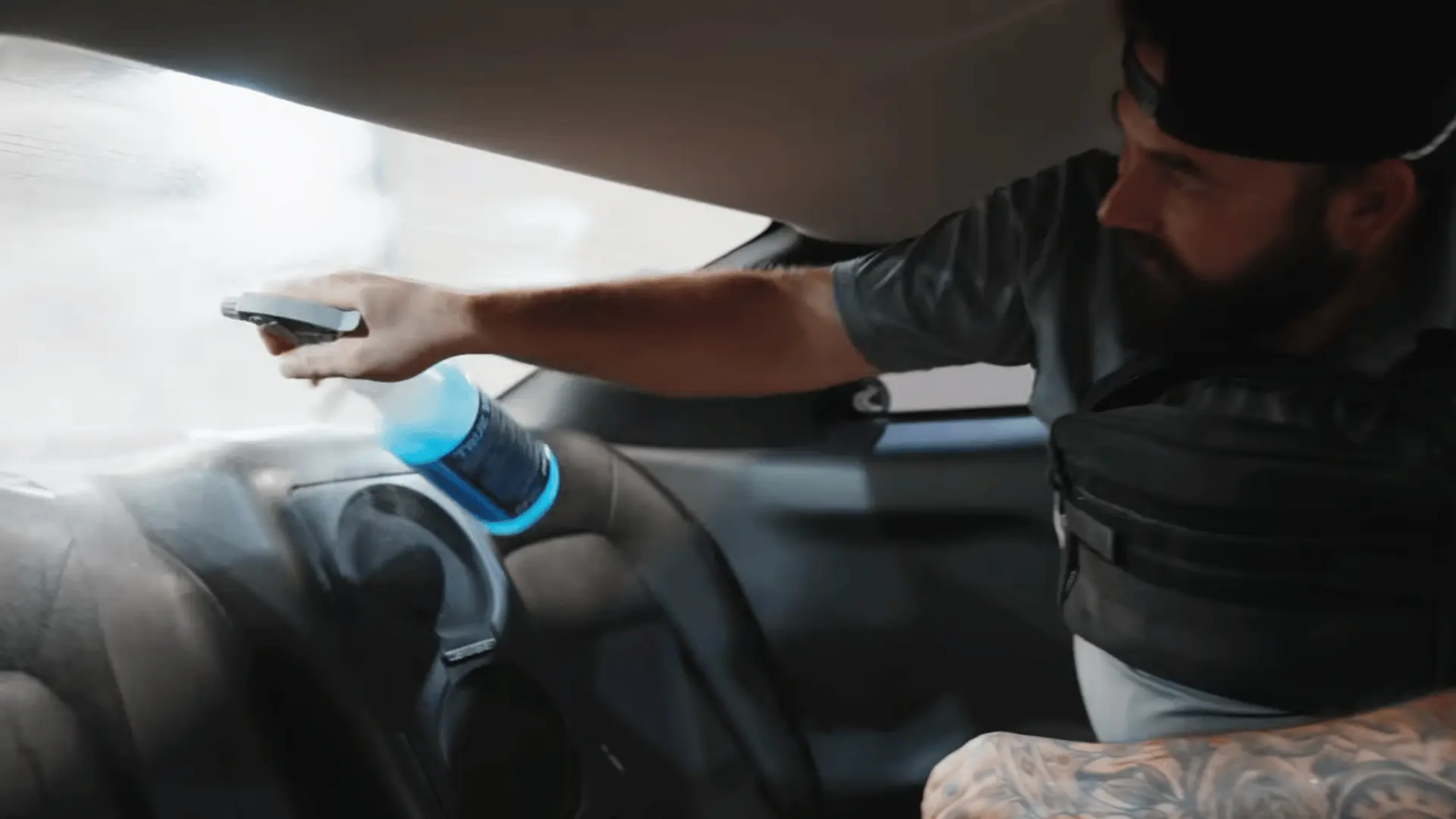 a bearded worker sprays cleaning solution across the rear windshield before applying dark window film