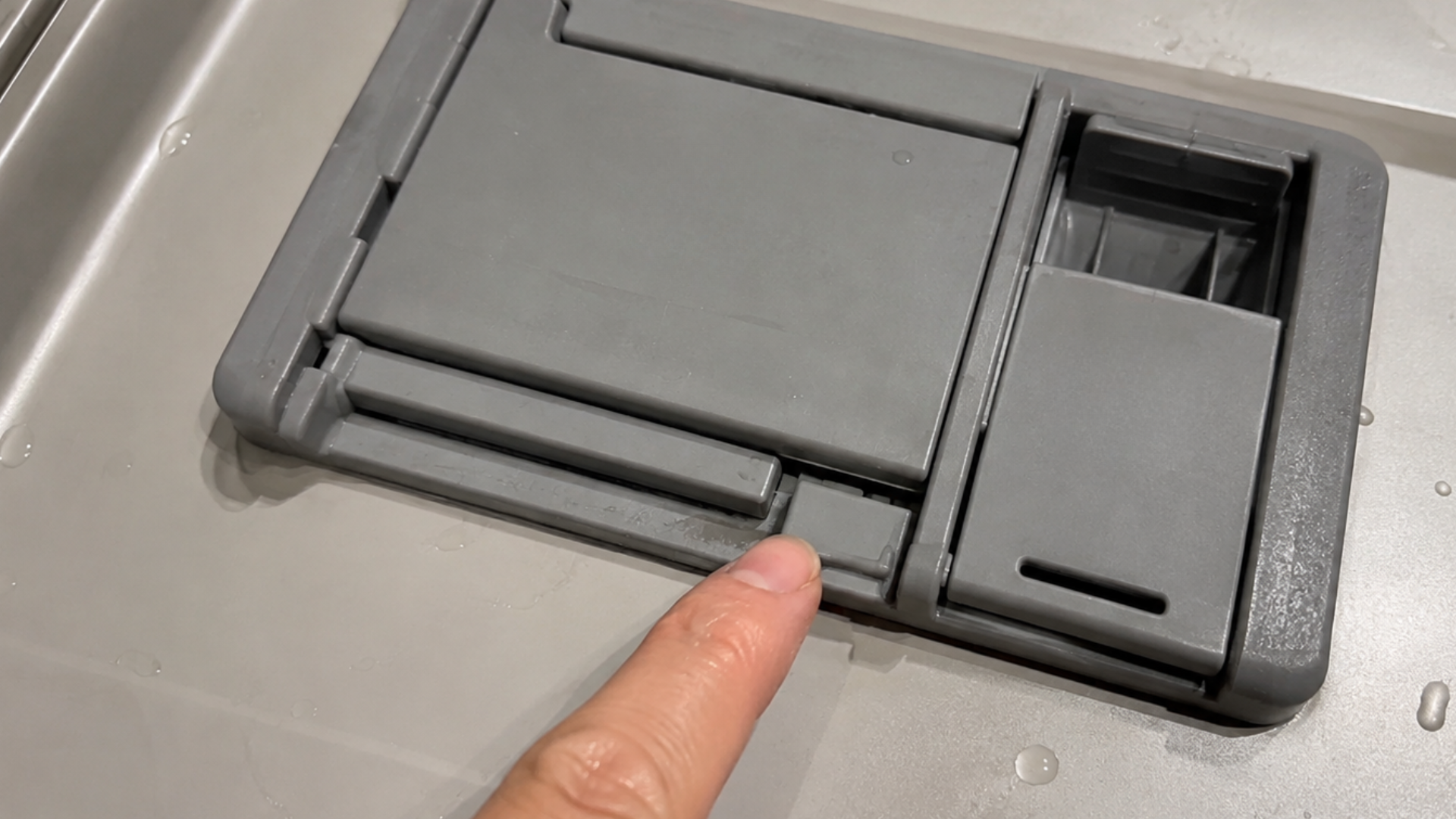 finger pressing a stuck dishwasher detergent dispenser latch that prevents the compartment from opening