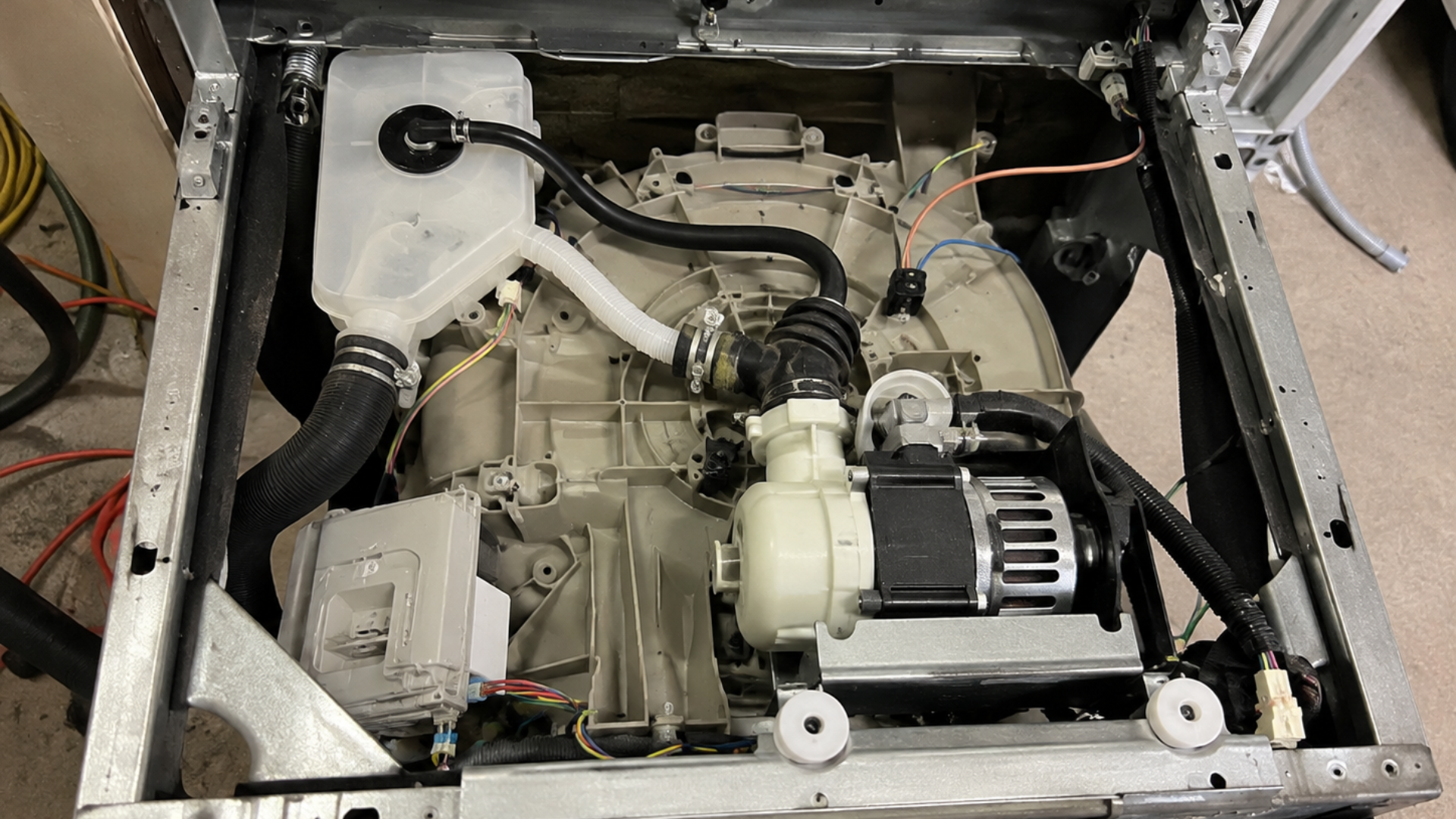 exposed dishwasher underside showing the pump hoses wiring motor and other internal components