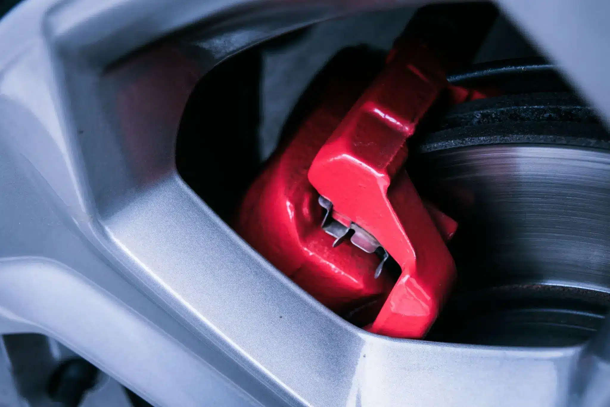Red brake caliper in close-up view of car wheel with metallic gray rim