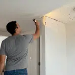 homeowner inspecting early termite signs along a ceiling corner with a flashlight