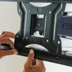 hands tightening the lower rail of a television wall bracket