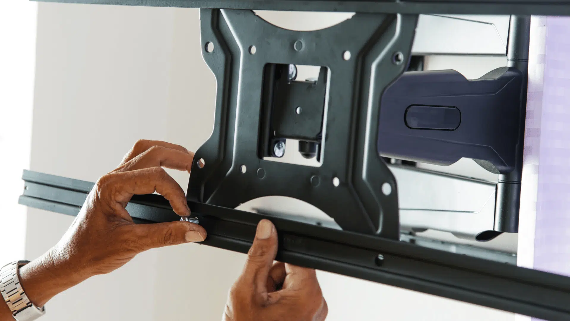 hands tightening the lower rail of a television wall bracket