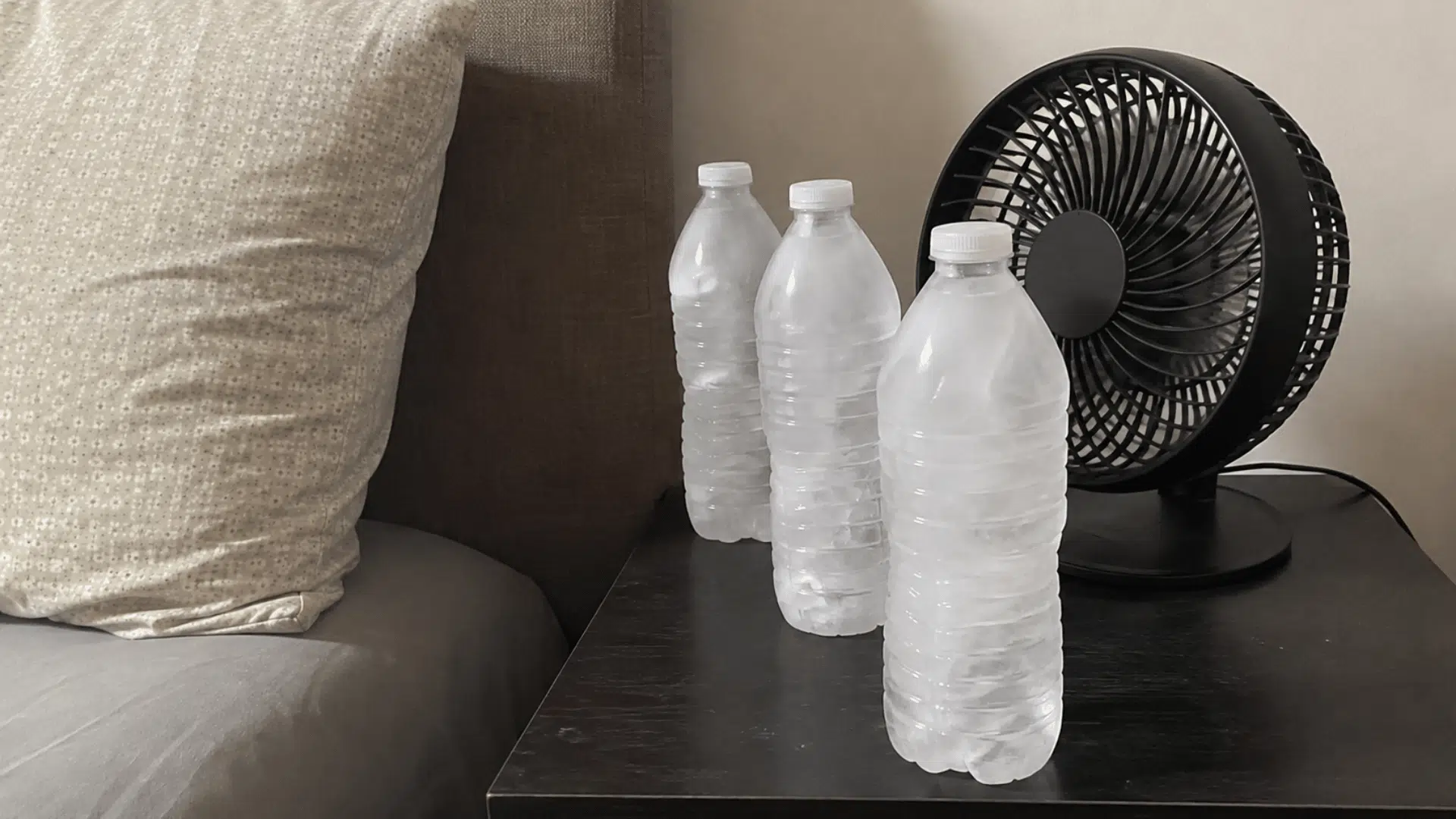 frozen water bottles placed in front of a small fan beside a bed to circulate cooler air nearby