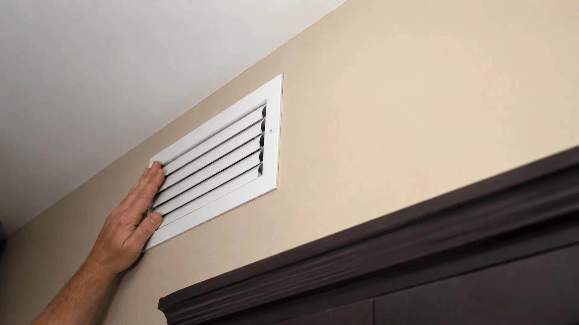 hand checking a wall air vent near the ceiling to manage airflow and reduce unwanted heat in the room
