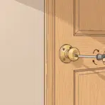 hand using a screwdriver to tighten a loose brass doorknob on a door (1)