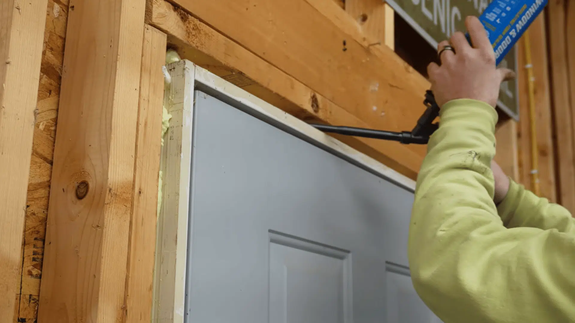 homeowner sealing gaps around studs pipes and window edges in an unfinished garage before adding insulation