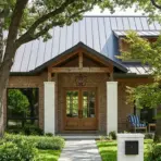 brick suburban home with a gray roof, double entry doors, covered porch, mature trees, shrubs, and a front walkway
