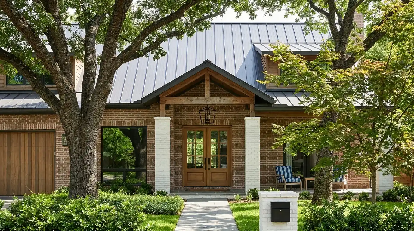 brick suburban home with a gray roof, double entry doors, covered porch, mature trees, shrubs, and a front walkway