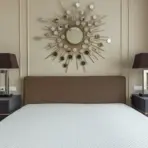 Modern bedroom with brown headboard and sunburst mirror above, flanked by two dark bedside tables