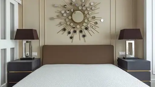 Modern bedroom with brown headboard and sunburst mirror above, flanked by two dark bedside tables