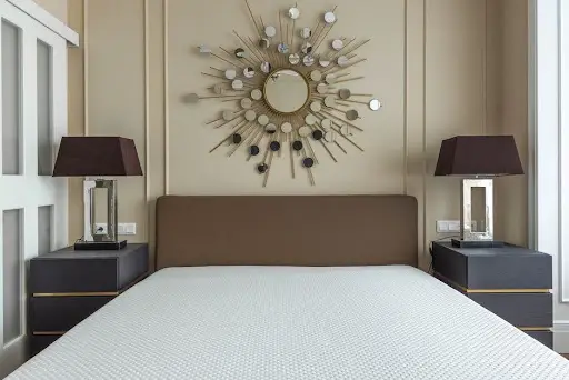 Modern bedroom with brown headboard and sunburst mirror above, flanked by two dark bedside tables