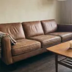 brown leather couch with a throw blanket in a cozy living room near a sunlit window