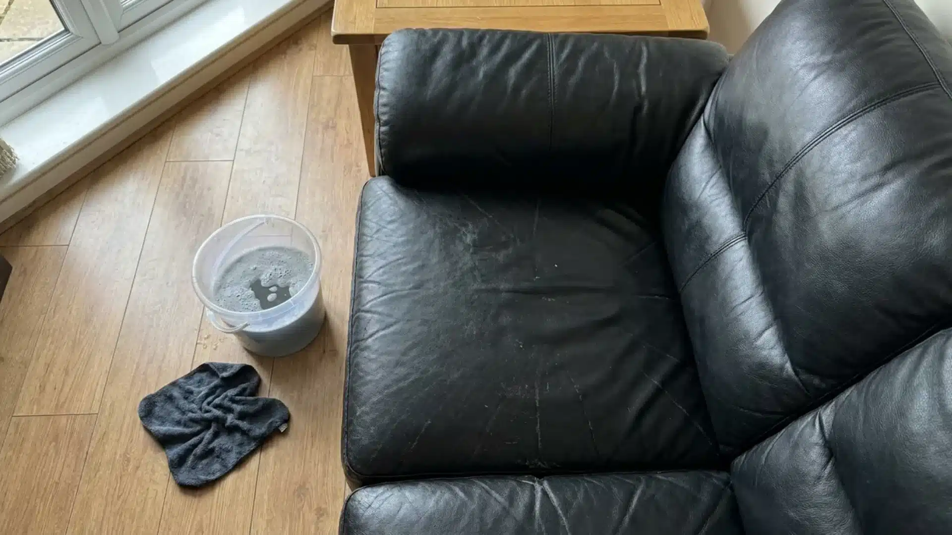 black leather couch cushion with a bucket of soapy water and a cloth resting nearby