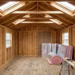 unfinished wooden shed interior with exposed framing, skylights, windows, rolled insulation, and construction materials