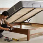 person tightening a corner bolt on a wooden bed frame to stop it squeaking