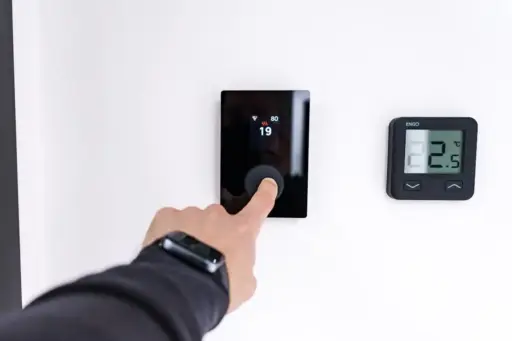 Finger pressing digital thermostat on white wall displaying temperature settings