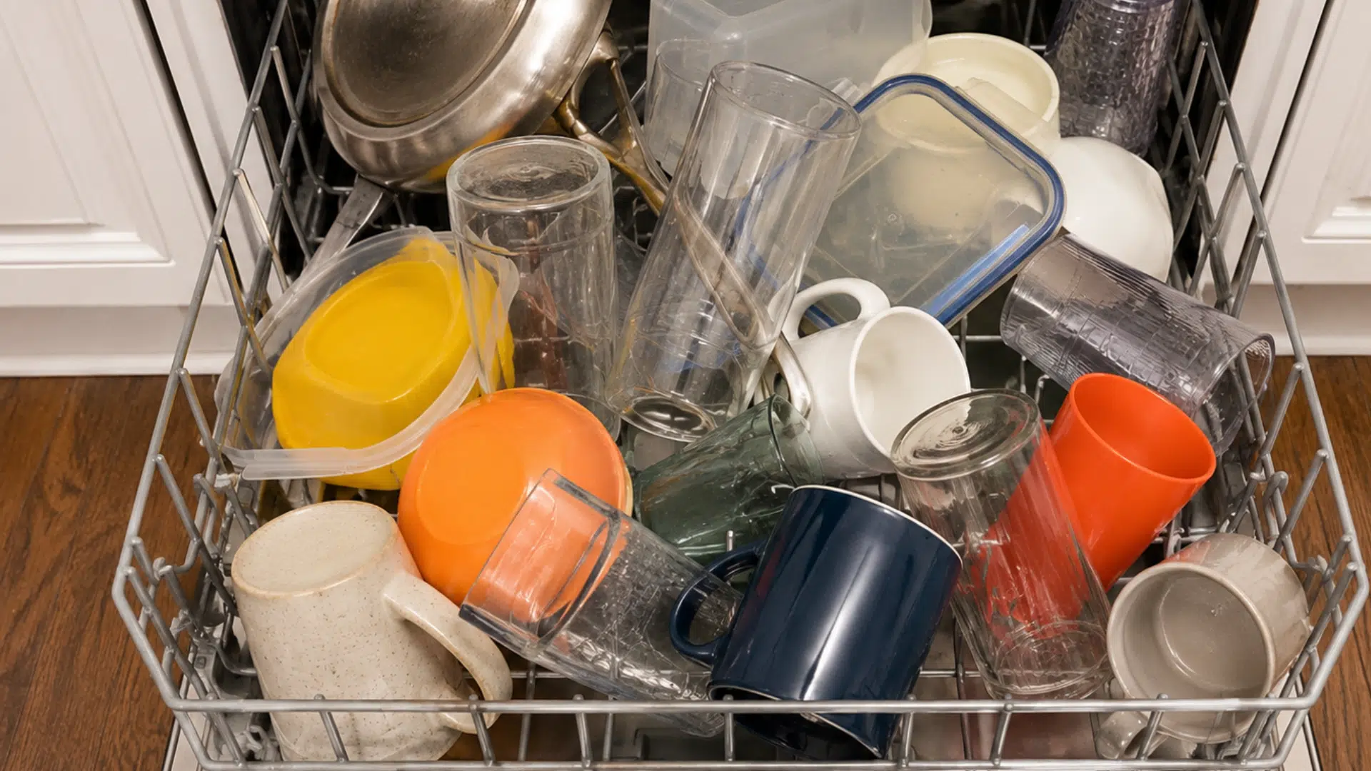 overloaded dishwasher rack with cups glasses cookware and containers placed in an incorrect arrangement