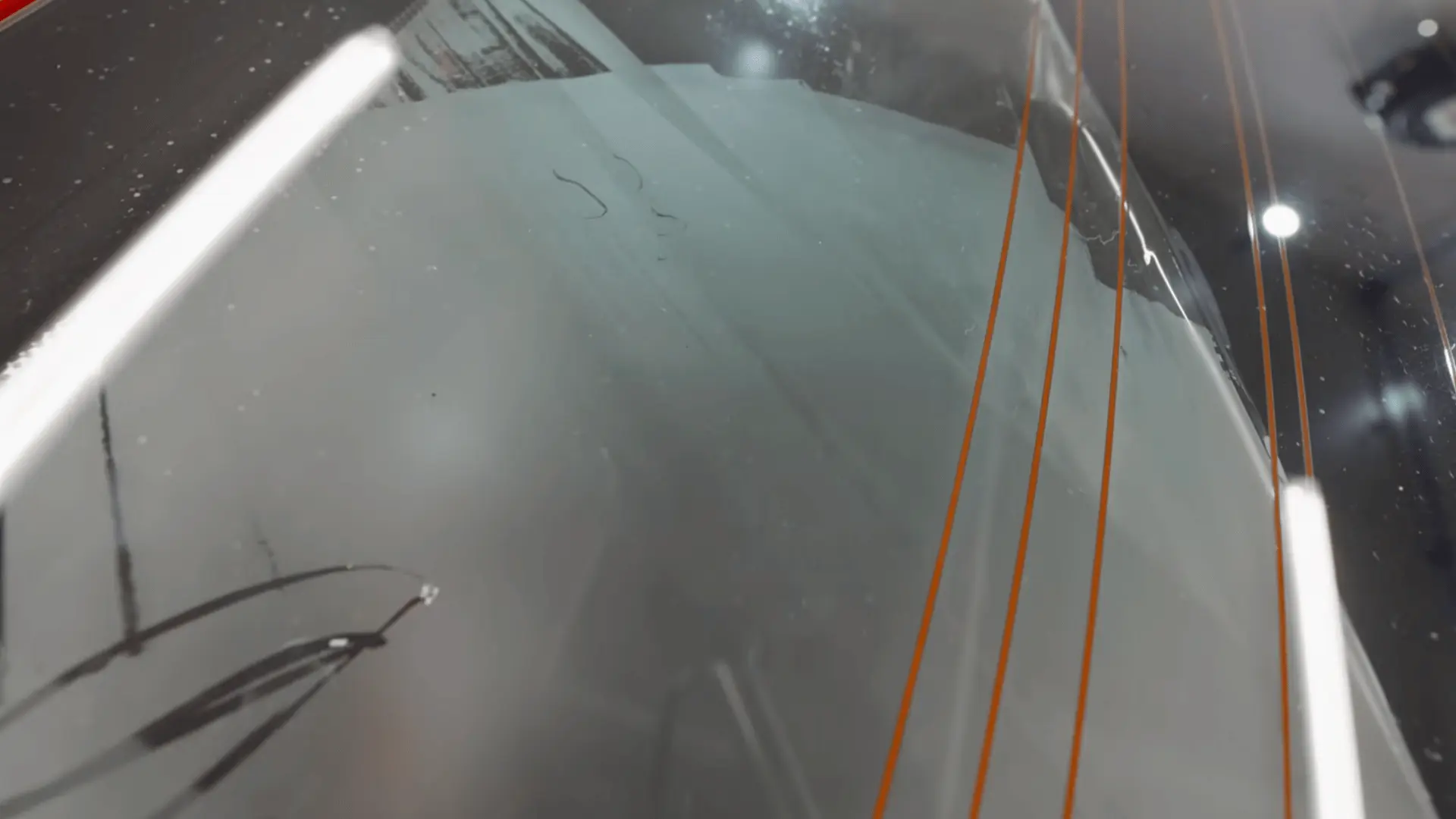 a close view shows wet window film with orange guide lines fitted against the rear windshield of a car