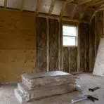 unfinished wood shed with wall insulation roof baffles plywood panels and diy tools on the floor