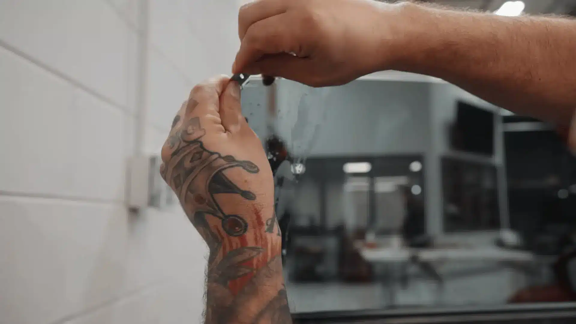 tattooed hands attach a small black clip to the upper edge of a wet car window inside an automotive workshop