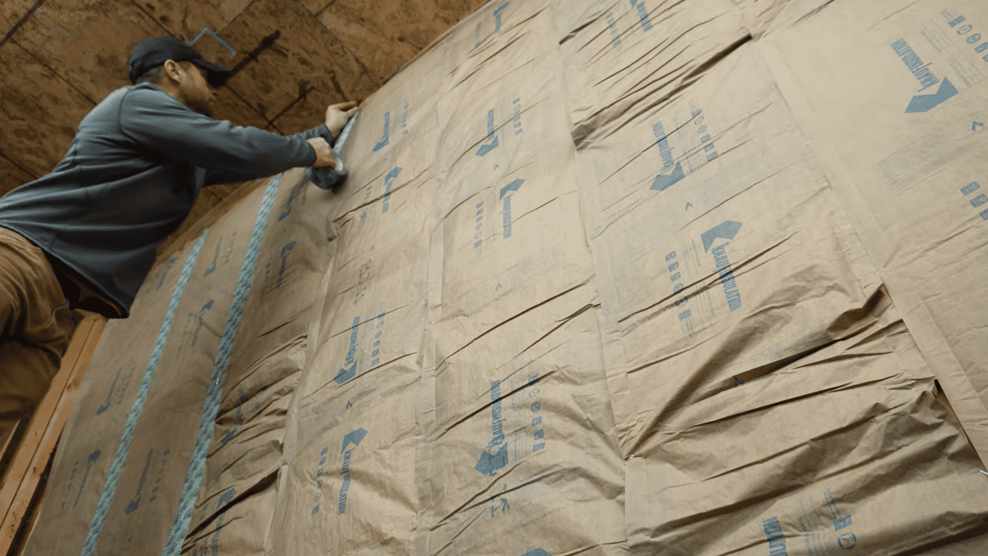 man installing faced fiberglass batt insulation across finished garage wall cavities before adding drywall