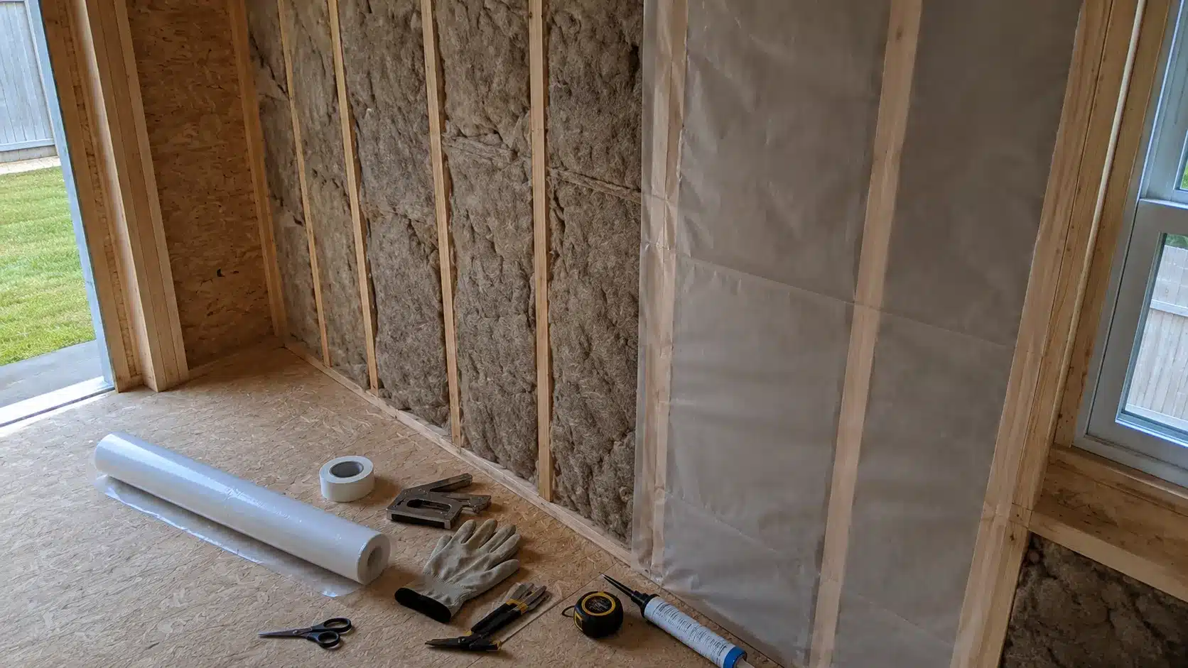 vapor control materials arranged on the floor beside an insulated shed wall with membrane partly installed