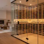 Glass-enclosed wine cellar with wooden racks in modern living room with fireplace and beige sofa