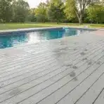 Swimming pool with wooden deck and lounge chairs in sunny backyard setting