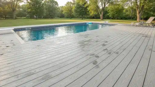 Swimming pool with wooden deck and lounge chairs in sunny backyard setting