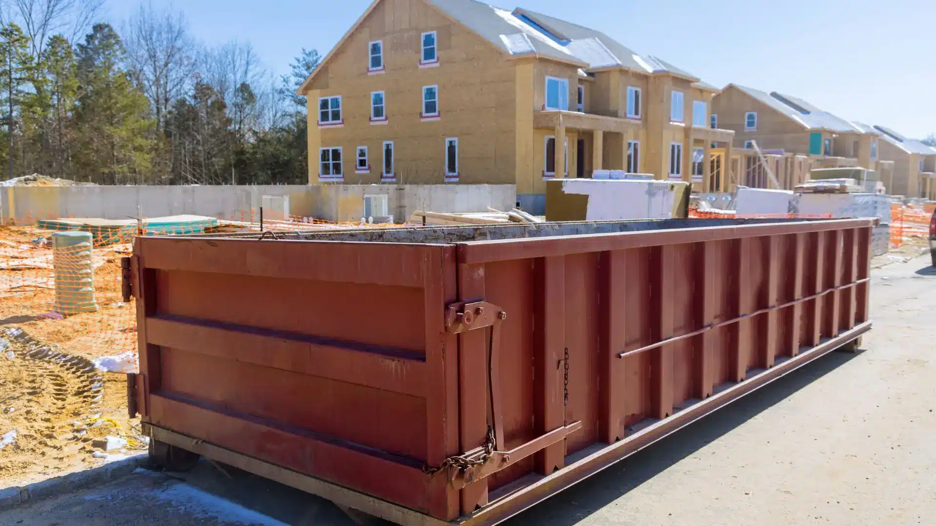 Large red dumpster on construction site with new houses under bright blue sky