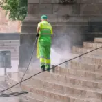 Worker in fluorescent uniform pressure washing stone steps outdoors