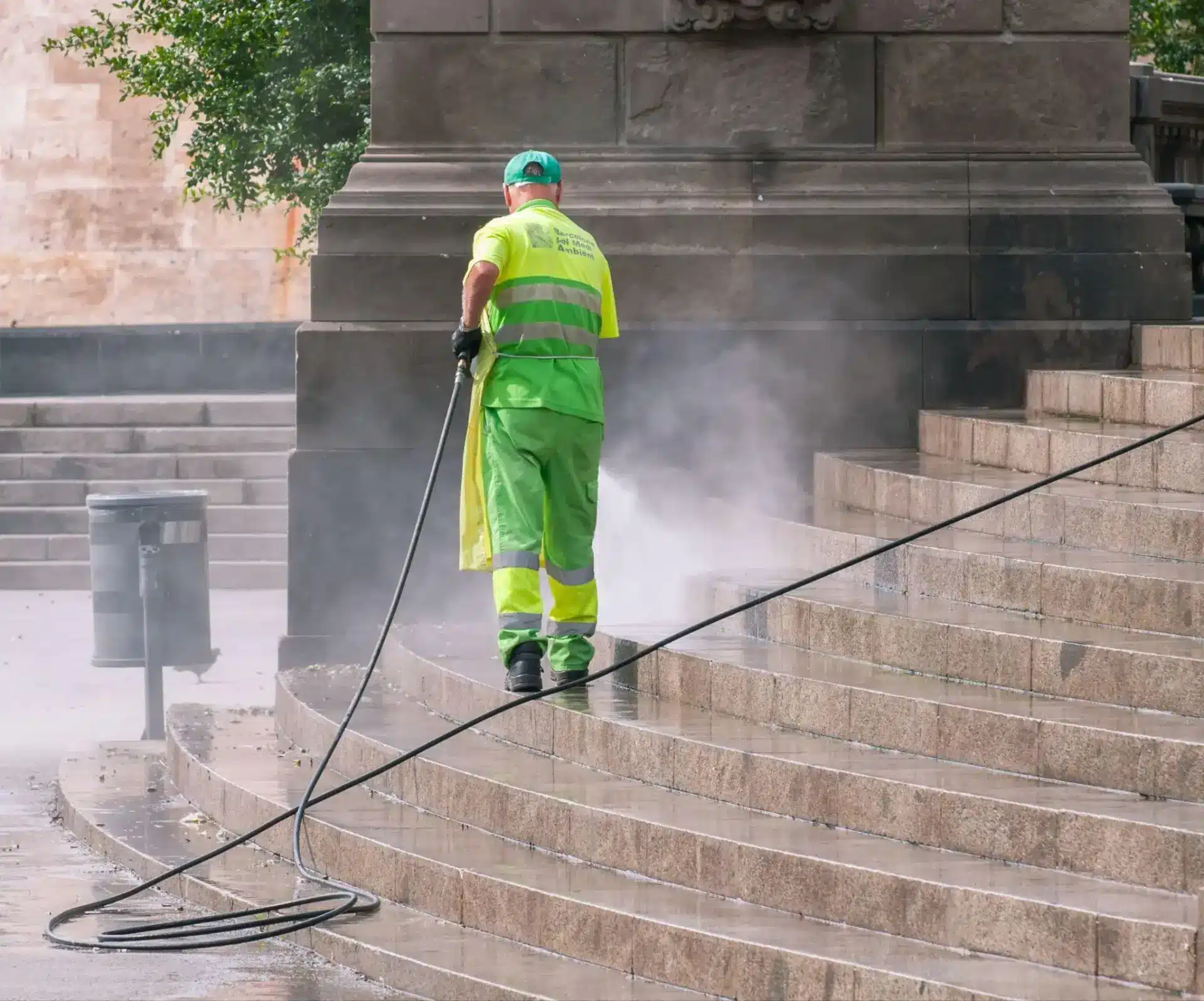 Worker in fluorescent uniform pressure washing stone steps outdoors