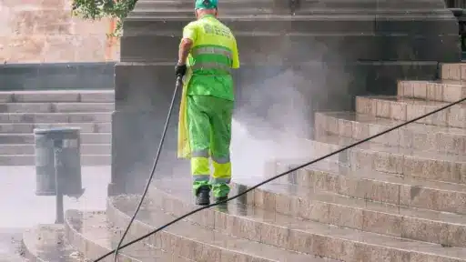 Worker in fluorescent uniform pressure washing stone steps outdoors