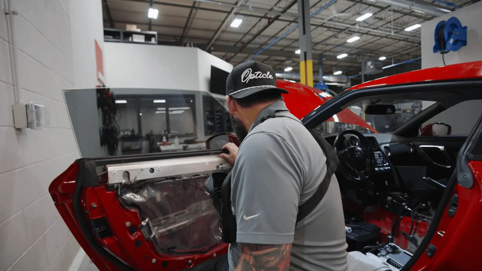 a technician inspects the exposed inner panel of a red car door inside a brightly lit automotive workshop