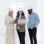 Three people in hard hats discussing plans on a laptop in a bright room