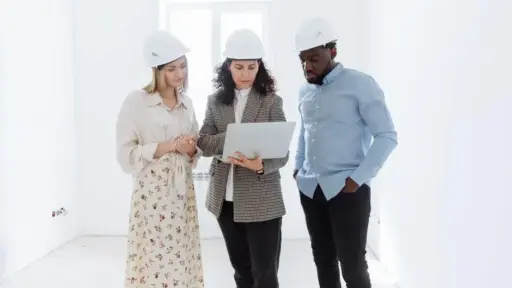 Three people in hard hats discussing plans on a laptop in a bright room