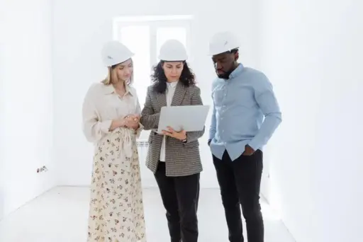 Three people in hard hats discussing plans on a laptop in a bright room