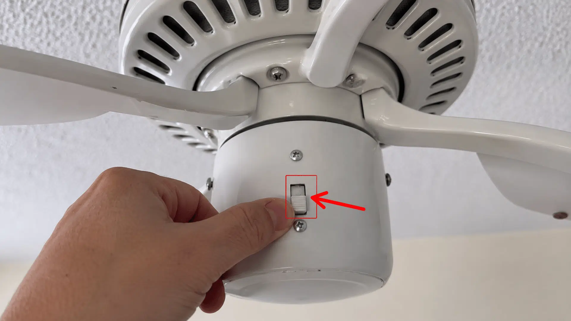 hand adjusting the reverse switch on a ceiling fan to change blade direction for better summer airflow