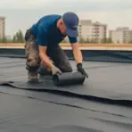 worker installing flat roof membrane material during rooftop waterproofing process