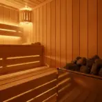 Warmly lit wooden sauna interior with bench and hot stones on heater