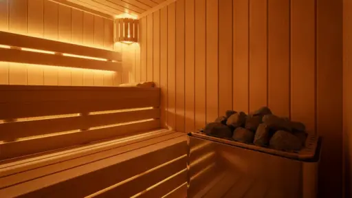 Warmly lit wooden sauna interior with bench and hot stones on heater