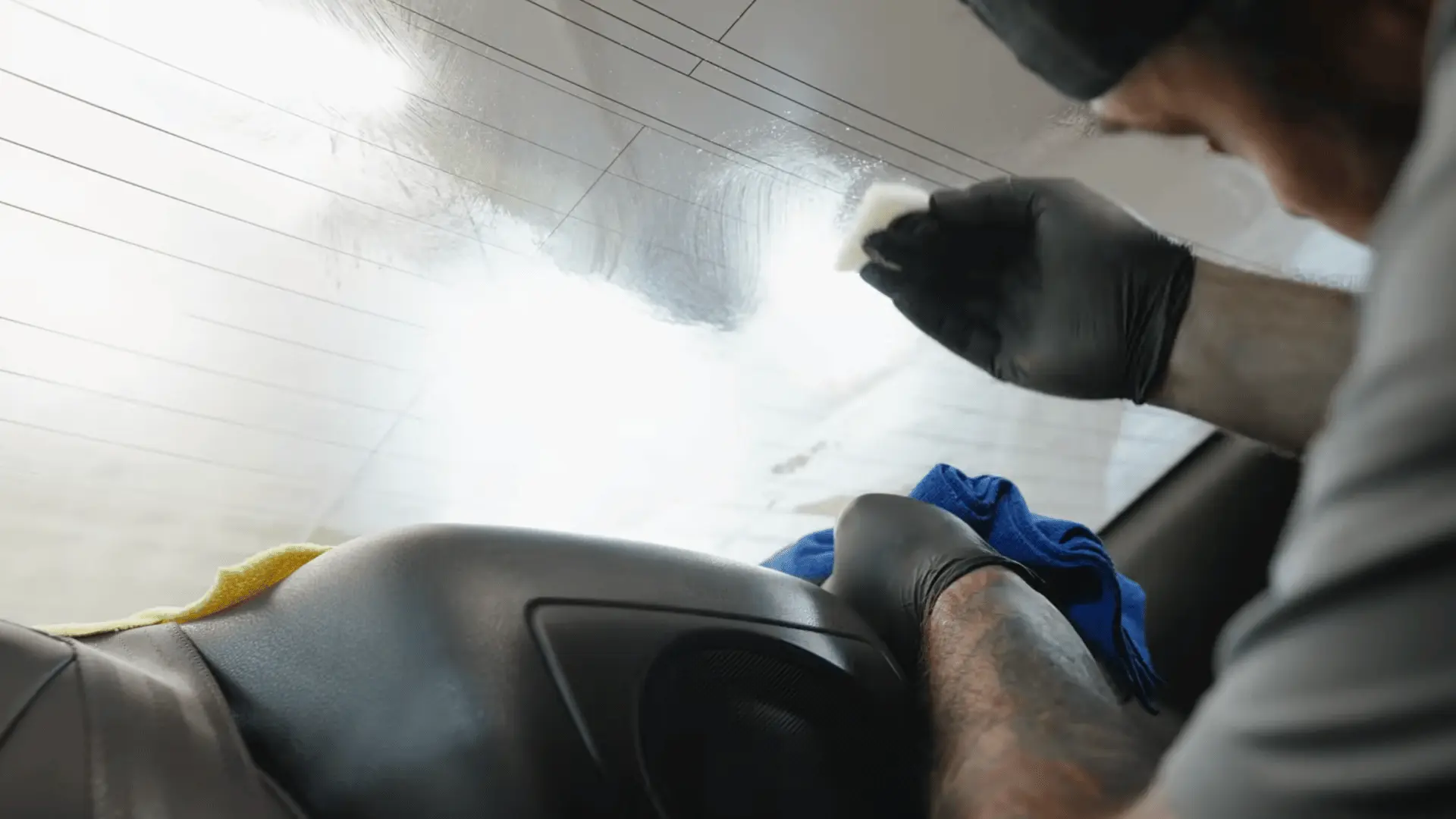 a gloved worker wipes and smooths the wet rear windshield with a small tool during window film installation