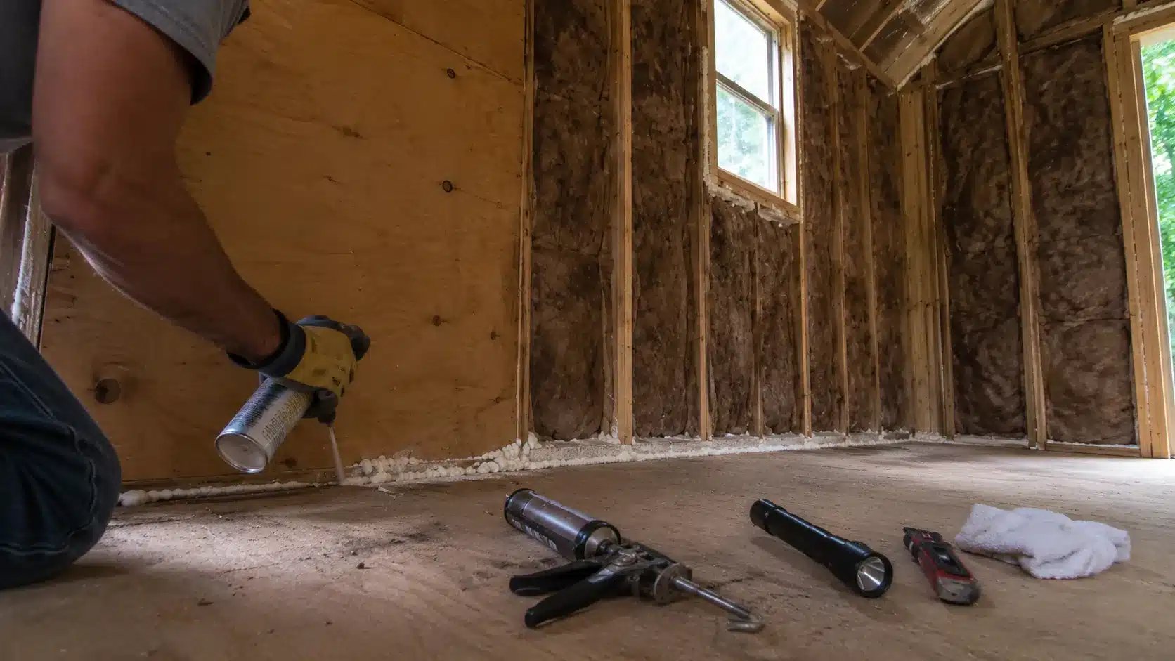 applying spray foam along the base of a shed wall to seal air gaps before insulation