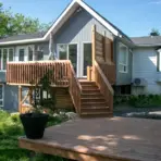 Wooden deck and staircase leading to a modern house with large windows and lush greenery